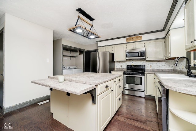 kitchen featuring pendant lighting, dark wood-type flooring, washing machine and dryer, a kitchen island, and stainless steel appliances