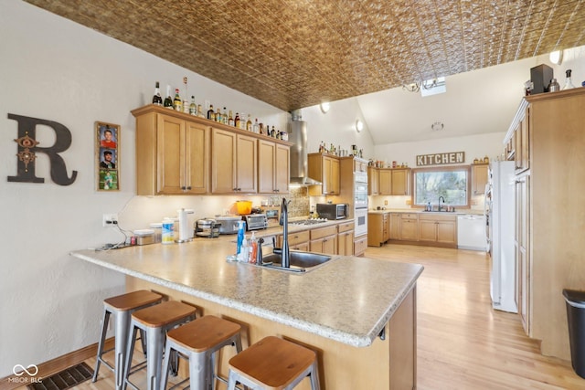 kitchen featuring sink, white appliances, kitchen peninsula, and wall chimney exhaust hood