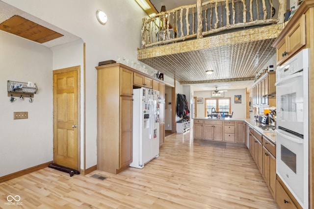 kitchen with light wood-type flooring, light brown cabinetry, white appliances, and kitchen peninsula