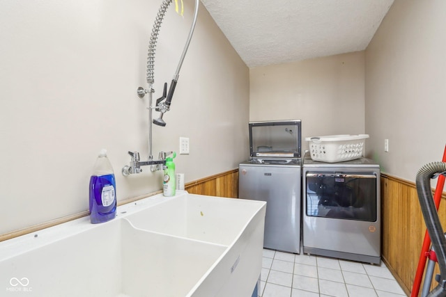 laundry area featuring washing machine and clothes dryer, sink, a textured ceiling, and wood walls