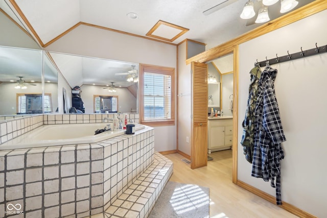 bathroom with lofted ceiling, wood-type flooring, vanity, tiled tub, and ceiling fan