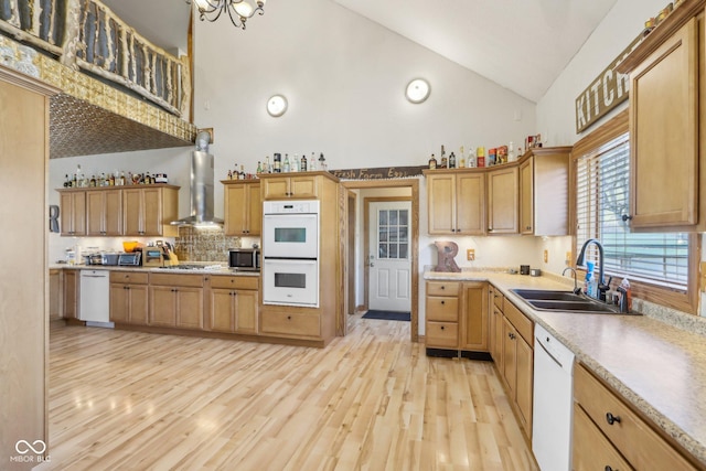 kitchen with high vaulted ceiling, sink, stainless steel appliances, wall chimney range hood, and light wood-type flooring