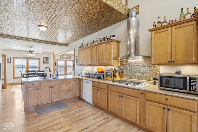 kitchen with sink, decorative backsplash, kitchen peninsula, wall chimney range hood, and white appliances