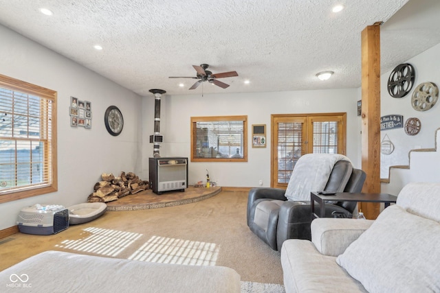 living room featuring carpet floors, a wood stove, a textured ceiling, and ceiling fan