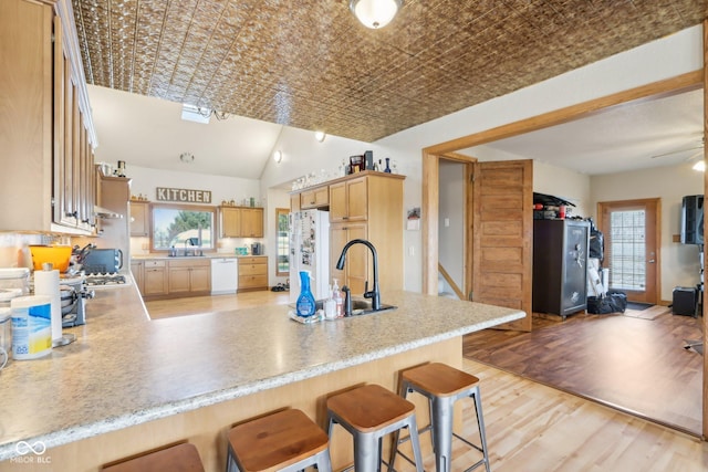 kitchen with sink, white appliances, a breakfast bar area, kitchen peninsula, and light wood-type flooring