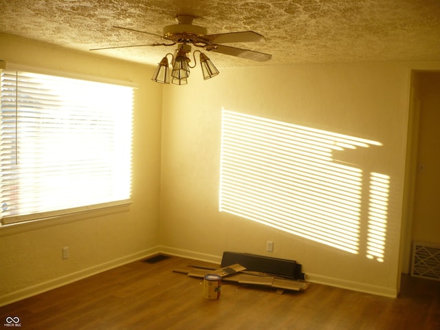 empty room featuring ceiling fan, hardwood / wood-style floors, a healthy amount of sunlight, and a textured ceiling