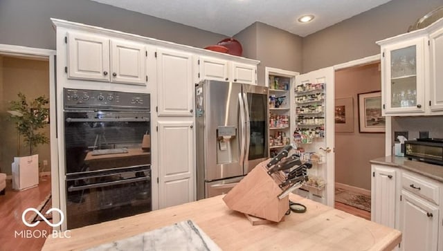 kitchen with double oven, stainless steel fridge with ice dispenser, white cabinetry, and wood-type flooring