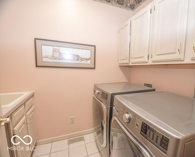 washroom featuring washing machine and dryer, light tile patterned floors, and cabinets