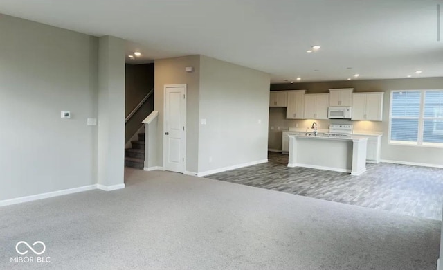 kitchen featuring white cabinetry, sink, white appliances, a kitchen island with sink, and carpet