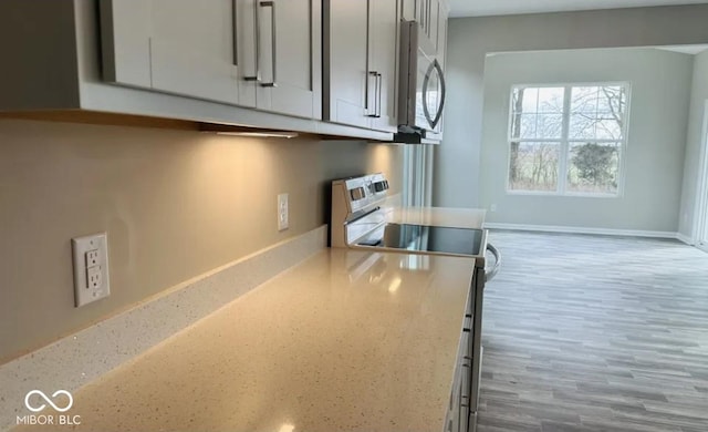 kitchen with appliances with stainless steel finishes, light wood-type flooring, and light stone counters