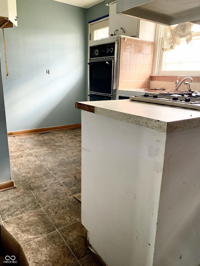 kitchen featuring decorative backsplash, dark tile patterned floors, black double oven, and exhaust hood