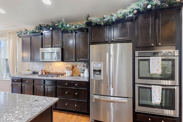 kitchen with stainless steel appliances, light stone counters, backsplash, light hardwood / wood-style floors, and dark brown cabinets