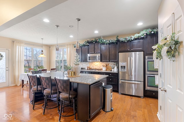 kitchen featuring a center island, hanging light fixtures, light hardwood / wood-style flooring, appliances with stainless steel finishes, and dark brown cabinetry