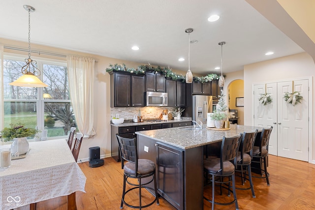 kitchen featuring a breakfast bar, hanging light fixtures, light hardwood / wood-style flooring, an island with sink, and stainless steel appliances