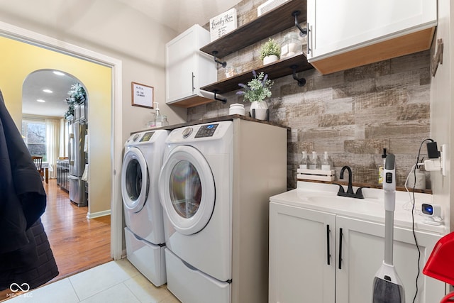 clothes washing area with separate washer and dryer, sink, light tile patterned floors, and cabinets