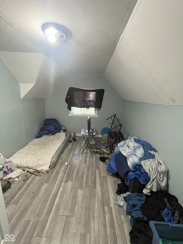 bedroom with a textured ceiling, light hardwood / wood-style floors, and lofted ceiling