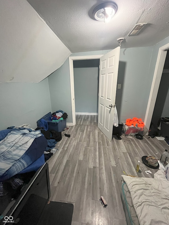 bedroom featuring wood-type flooring, a textured ceiling, and vaulted ceiling