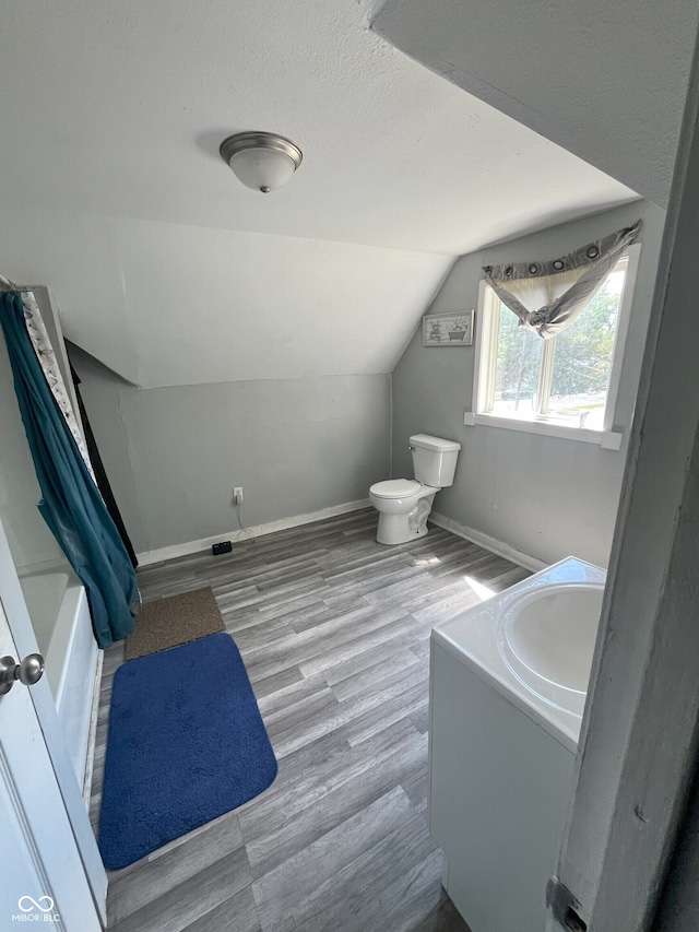 full bathroom featuring hardwood / wood-style floors, vanity, shower / bath combo, lofted ceiling, and toilet