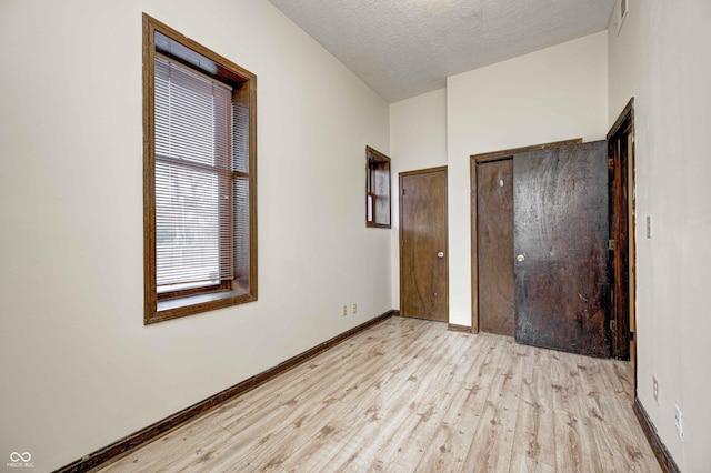 unfurnished bedroom with lofted ceiling, light hardwood / wood-style floors, and a textured ceiling