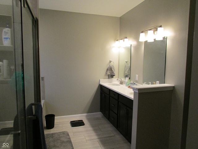 full bathroom with wood finish floors, a sink, baseboards, double vanity, and a stall shower