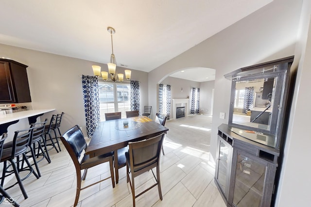 dining room featuring lofted ceiling, a healthy amount of sunlight, a chandelier, and a glass covered fireplace