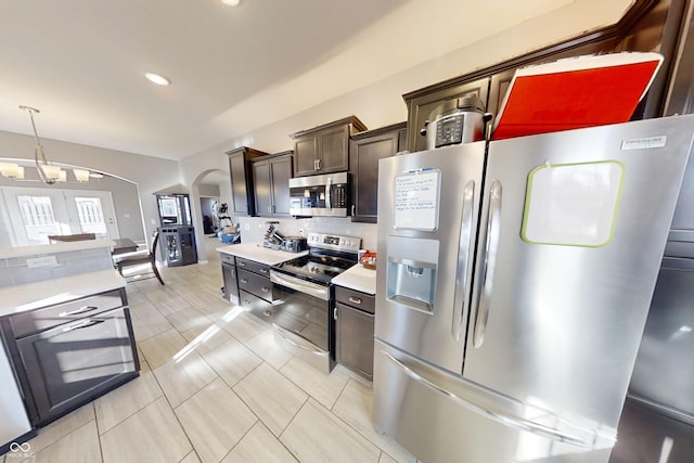 kitchen featuring arched walkways, light countertops, appliances with stainless steel finishes, dark brown cabinets, and decorative backsplash