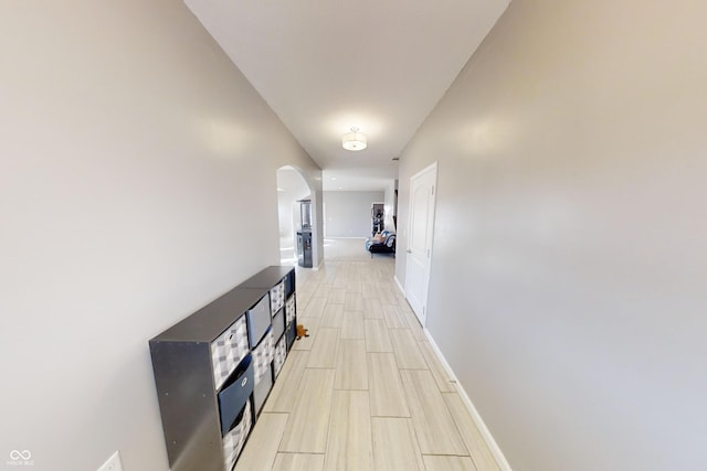 corridor with wood tiled floor, arched walkways, and baseboards