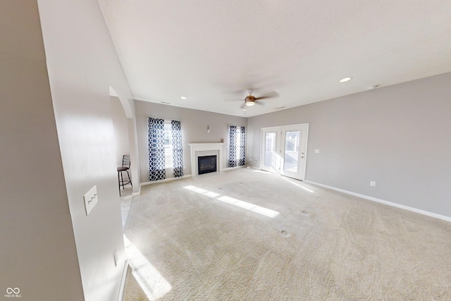 unfurnished living room with baseboards, a glass covered fireplace, a ceiling fan, and light colored carpet