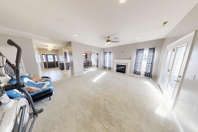 living room featuring arched walkways, recessed lighting, light colored carpet, visible vents, and a glass covered fireplace