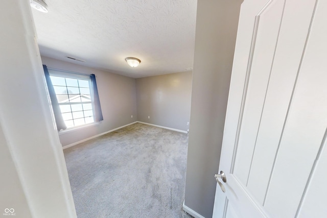 empty room featuring light carpet, visible vents, baseboards, and a textured ceiling