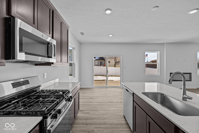 kitchen featuring sink, light hardwood / wood-style flooring, stainless steel appliances, light stone counters, and dark brown cabinetry