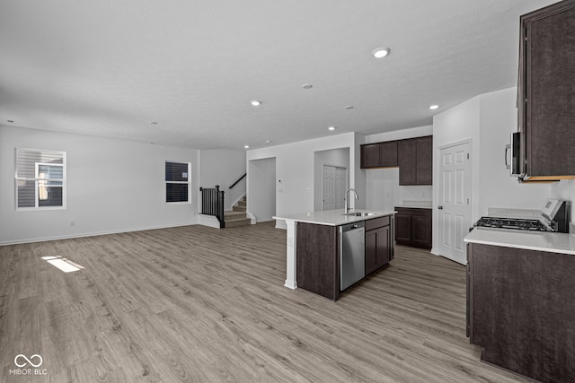 kitchen featuring appliances with stainless steel finishes, sink, dark brown cabinets, a center island with sink, and light wood-type flooring