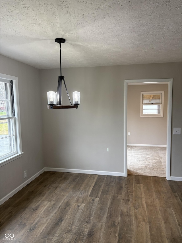 unfurnished dining area with a textured ceiling, dark wood-type flooring, and a notable chandelier