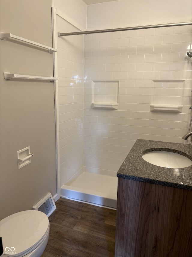 bathroom with tiled shower, hardwood / wood-style floors, vanity, and toilet