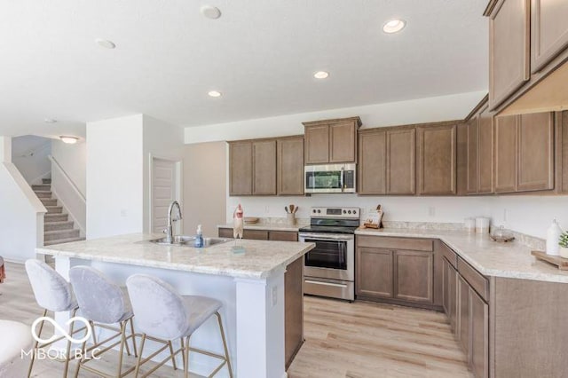 kitchen with light stone countertops, light wood-type flooring, stainless steel appliances, sink, and a center island with sink