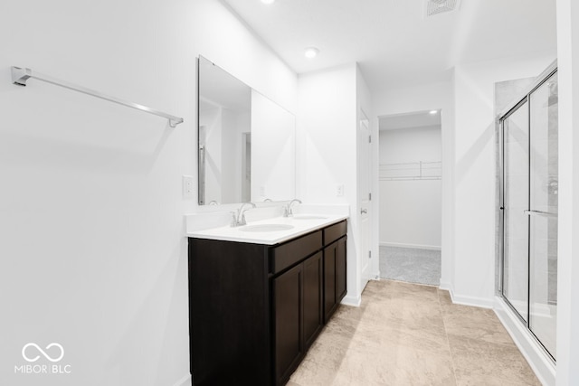 full bath featuring a spacious closet, double vanity, a stall shower, and a sink