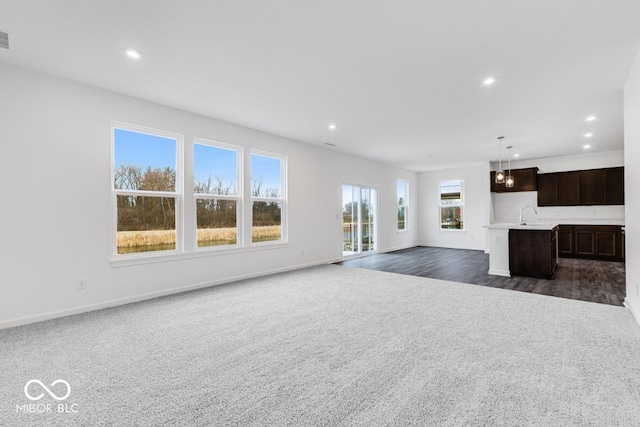 unfurnished living room with baseboards, dark carpet, a sink, and recessed lighting