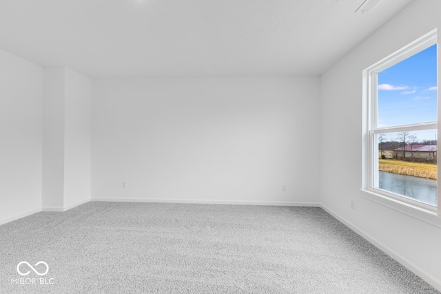 empty room with carpet flooring, a water view, and baseboards