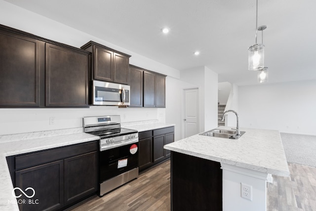 kitchen featuring appliances with stainless steel finishes, hanging light fixtures, a kitchen island with sink, dark brown cabinets, and a sink