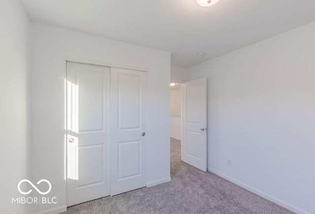 unfurnished bedroom with baseboards, a closet, and light colored carpet