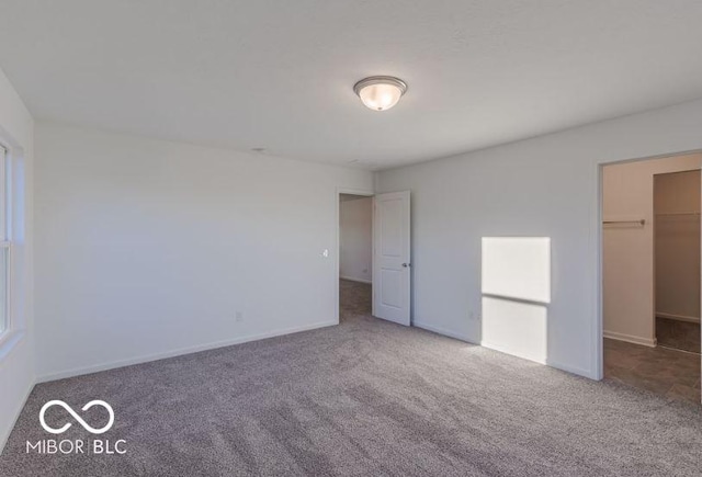 unfurnished bedroom with carpet flooring, a spacious closet, and baseboards