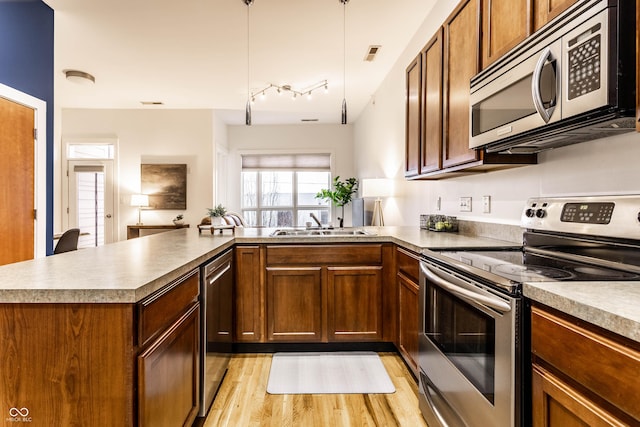 kitchen with sink, appliances with stainless steel finishes, kitchen peninsula, pendant lighting, and light hardwood / wood-style floors