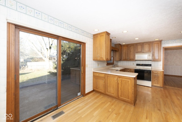 kitchen featuring kitchen peninsula, light wood-type flooring, white appliances, and sink