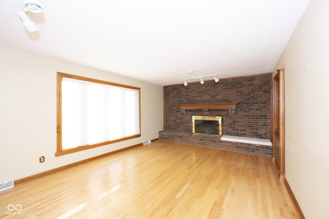 unfurnished living room with a fireplace, rail lighting, and light hardwood / wood-style floors