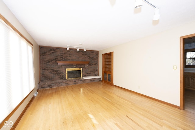 unfurnished living room featuring rail lighting, plenty of natural light, light wood-type flooring, and a fireplace