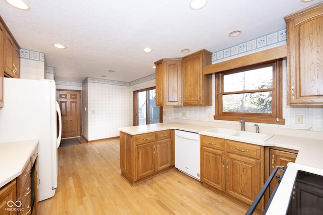 kitchen with white appliances, backsplash, sink, light hardwood / wood-style floors, and kitchen peninsula