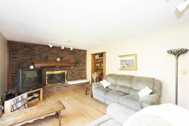 living room featuring a brick fireplace, track lighting, and light hardwood / wood-style flooring