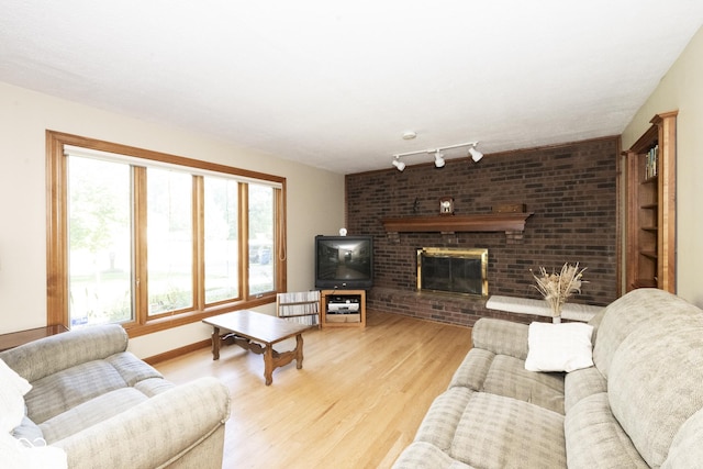 living room featuring rail lighting, light hardwood / wood-style floors, and a brick fireplace