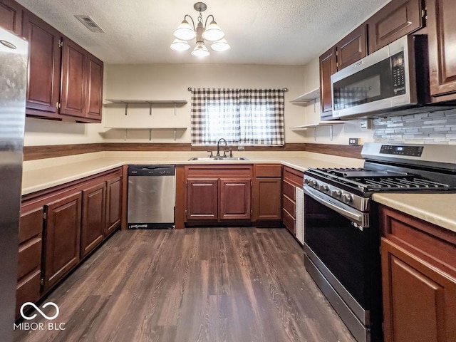 kitchen with sink, hanging light fixtures, stainless steel appliances, dark wood-type flooring, and a textured ceiling