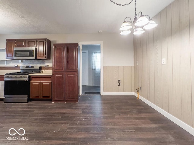 kitchen featuring dark wood-type flooring, appliances with stainless steel finishes, decorative light fixtures, and a notable chandelier